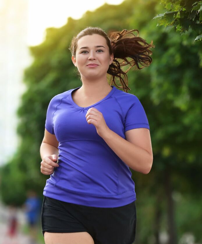 A woman jogs outside under the shade of some trees.
