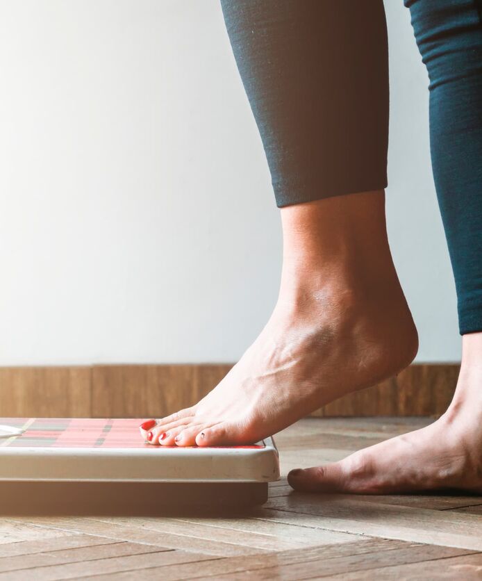 Side view of a woman’s lower legs stepping onto bathroom scales.