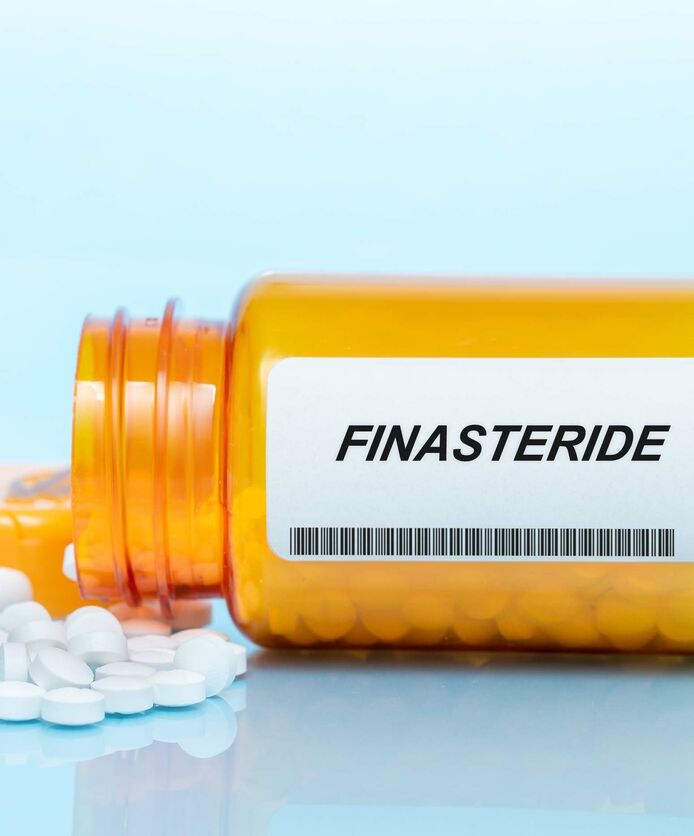 A bottle of finasteride pills on its side with the pills spilling out.