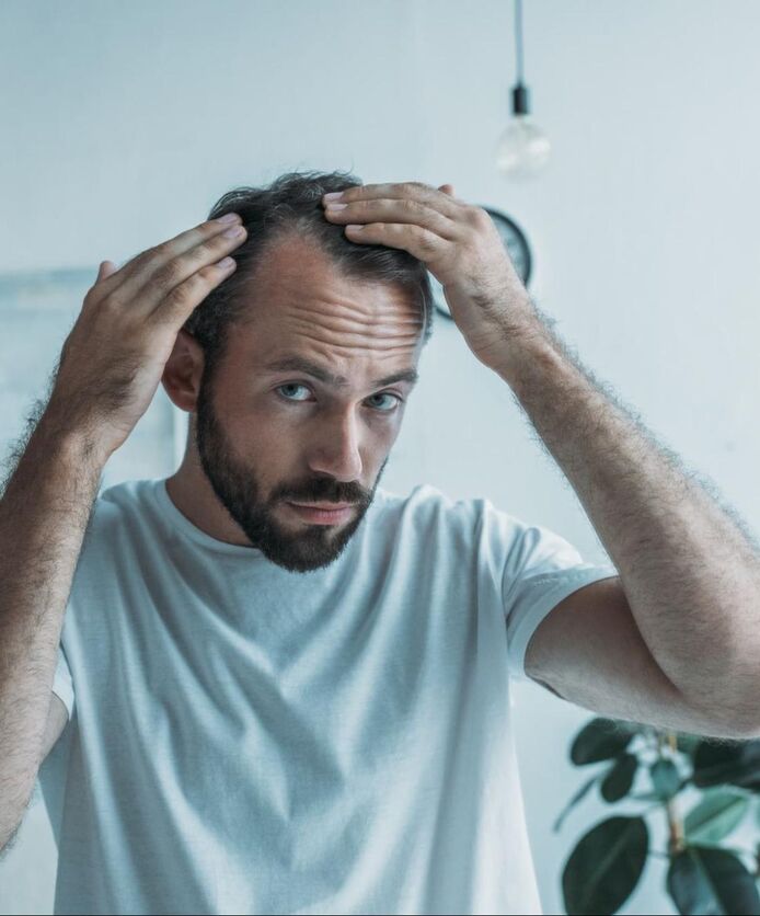 A man examines his receding hairline in the mirror.