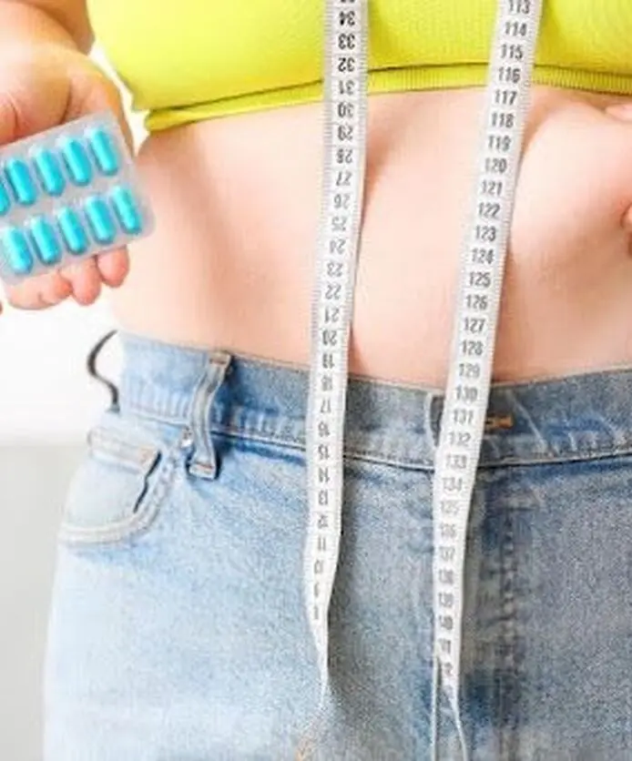 Woman holding weight loss pills while measuring her waist.