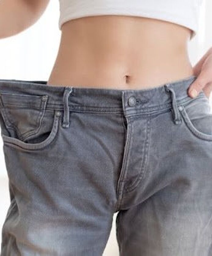 Woman holding loose jeans after weight loss.