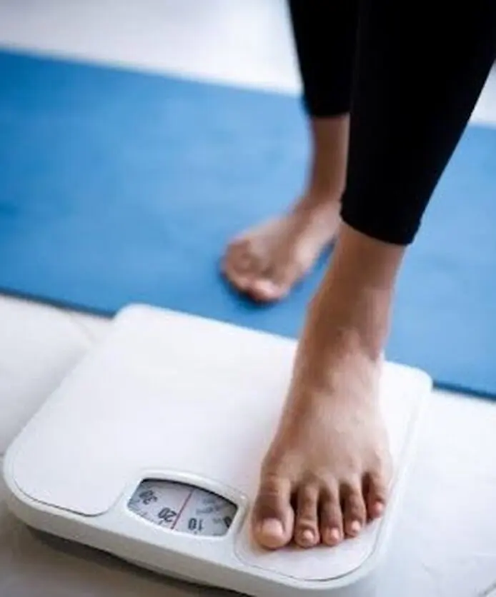 Person stepping on a weighing scale to track weight loss.