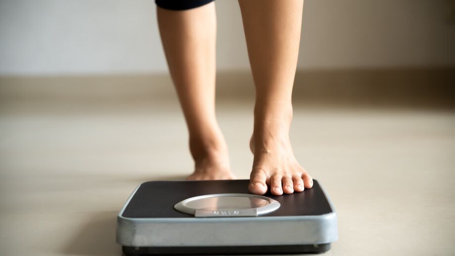 A woman wearing ¾ length leggings steps barefoot onto a set of digital scales.
