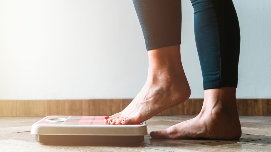 Side view of a woman’s lower legs stepping onto bathroom scales.