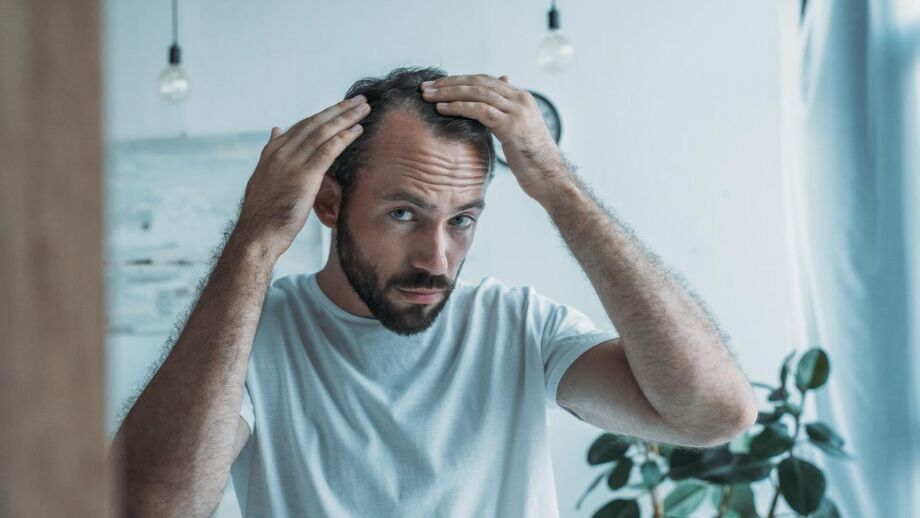 A man examines his receding hairline in the mirror.